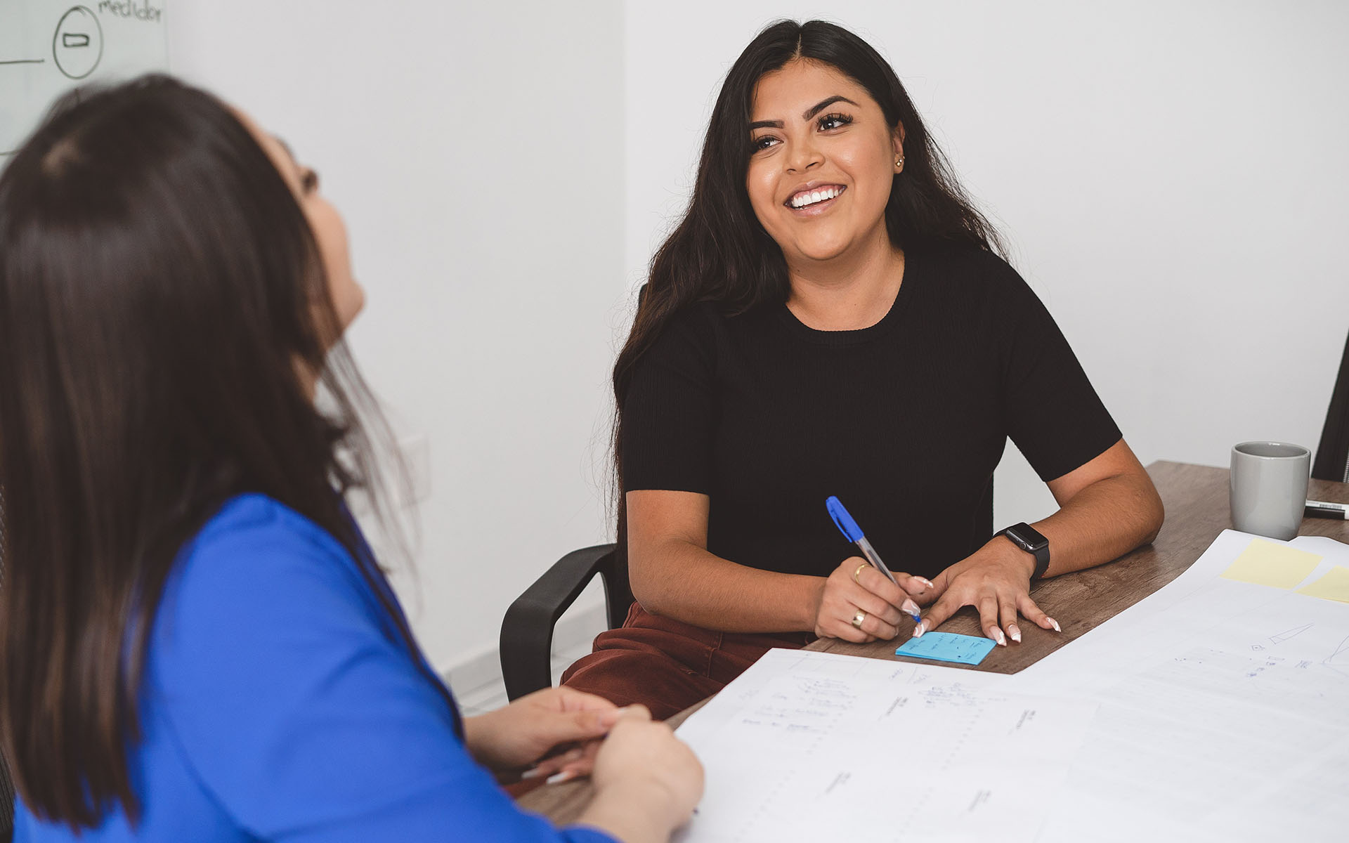 Two people sit at a table and speak with one another during a meeting.